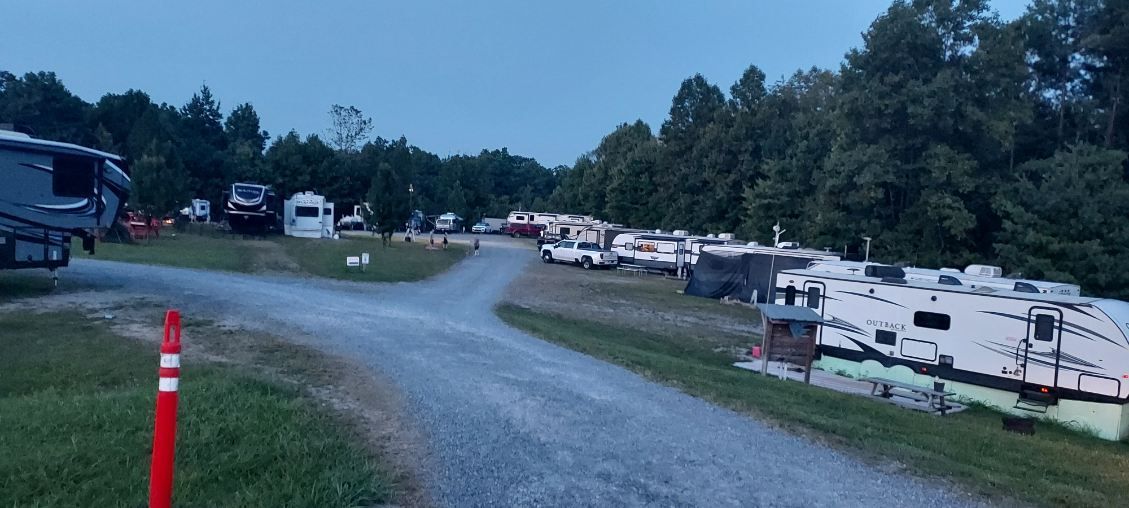Gravel road through an RV campground with parked campers and trees at dusk
