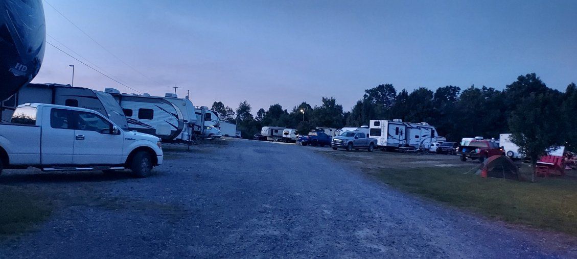 RV campground with parked trucks and campers along a gravel road at dusk