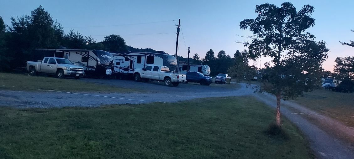RVs parked at a campground with trees and gravel sites at sunset