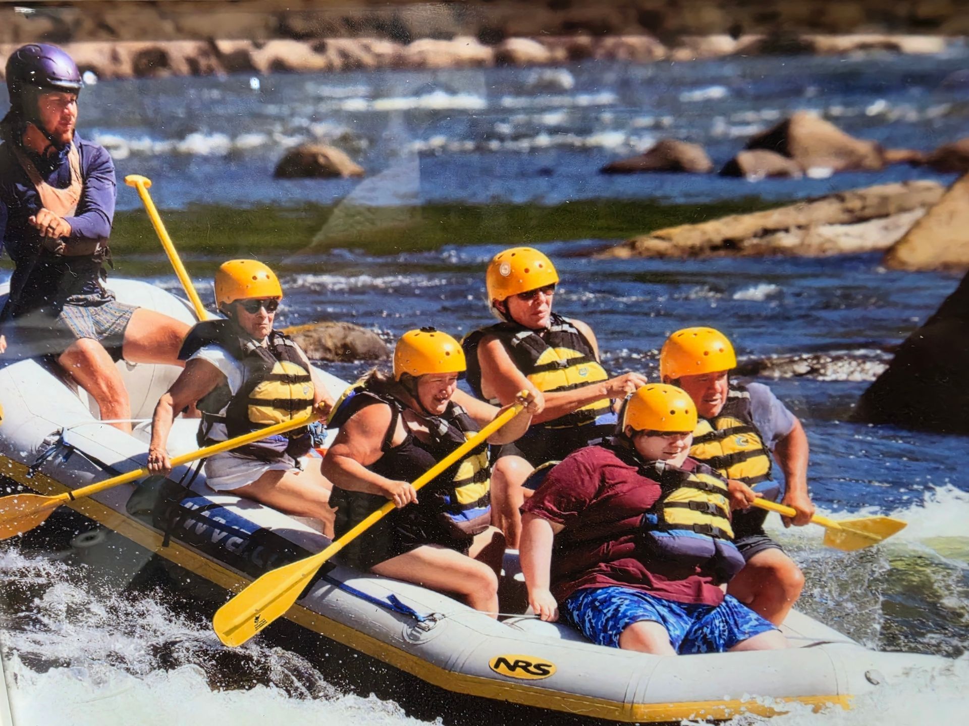 Rafting group in yellow helmets paddling through whitewater rapids