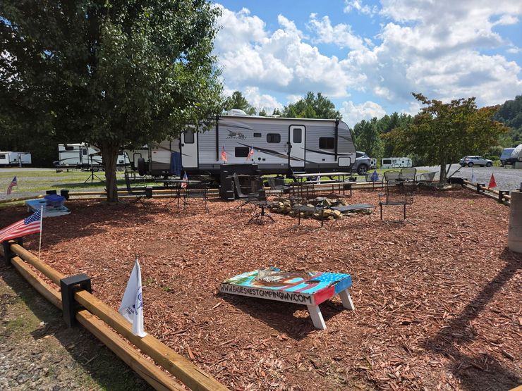 Camper trailer in a landscaped RV park with picnic table, mulch, trees, and blue sky