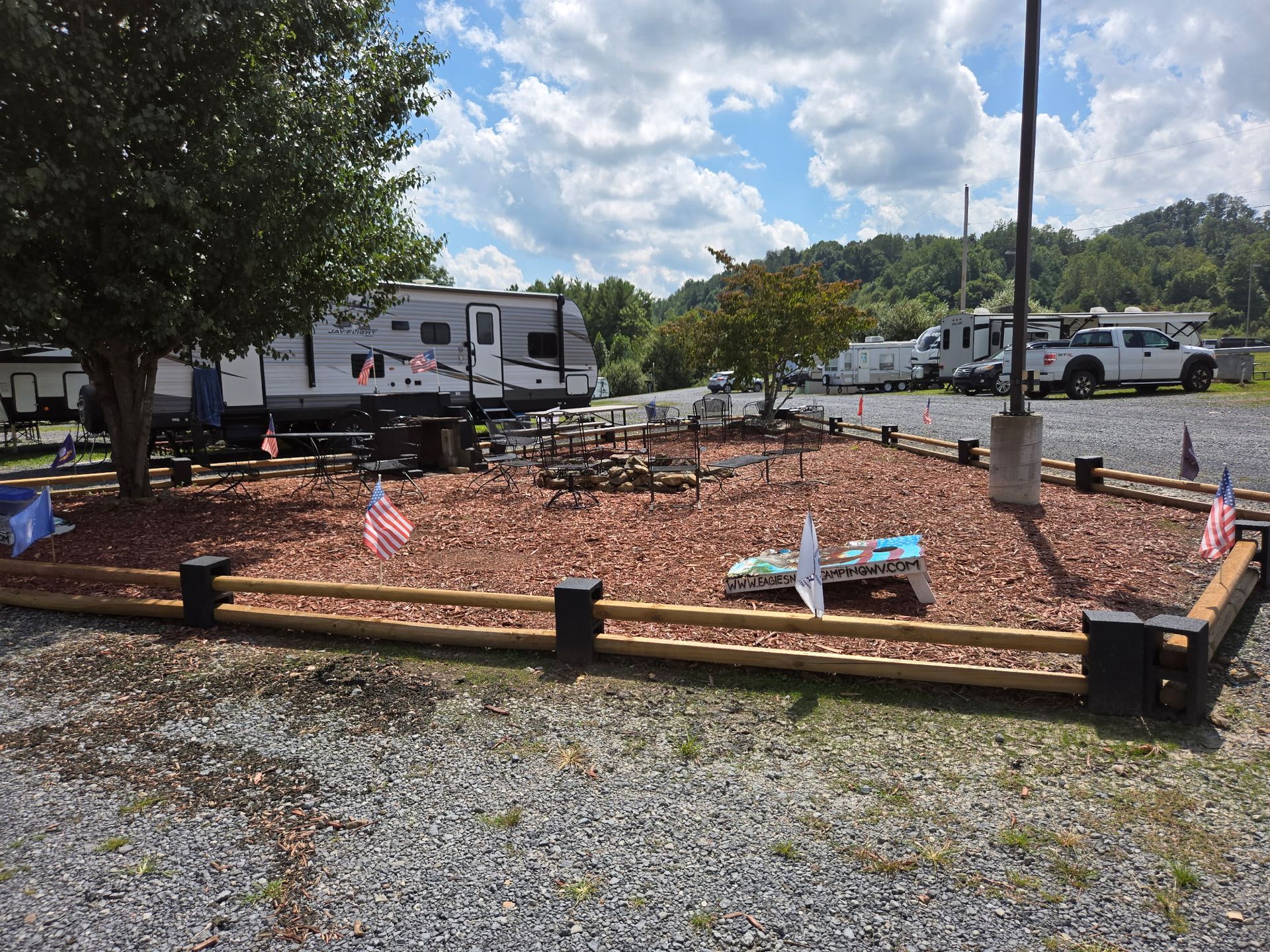 Memorial garden with small American flags, white stone markers, and RVs parked nearby under a partly cloudy sky
