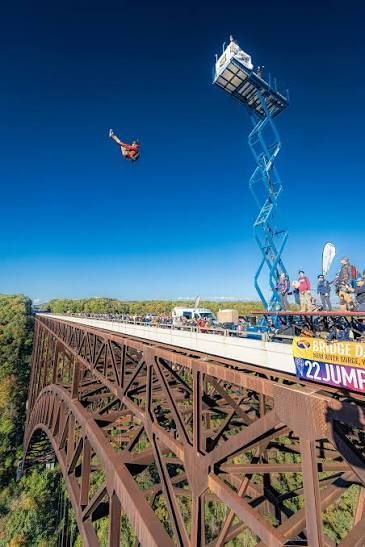 Bungee jumper soaring above a tall bridge beside a blue crane against a clear sky