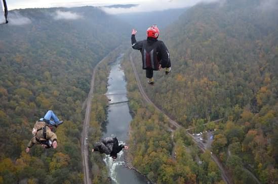 Three BASE jumpers in wingsuits soaring over a river canyon from a cliff