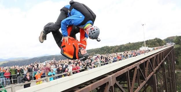 Two people mid-air during a bungee jump off a bridge, with a crowd watching below