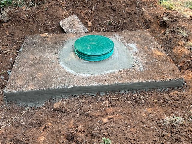 A septic tank with a green lid is sitting in the dirt.