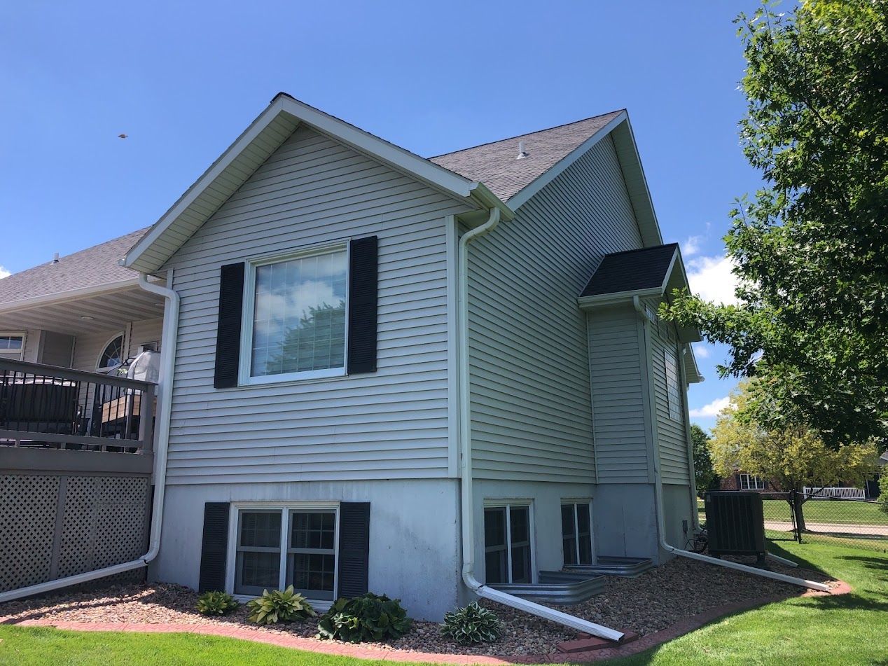 Exterior view of a two-story house with light siding, dark shutters, and a green lawn.