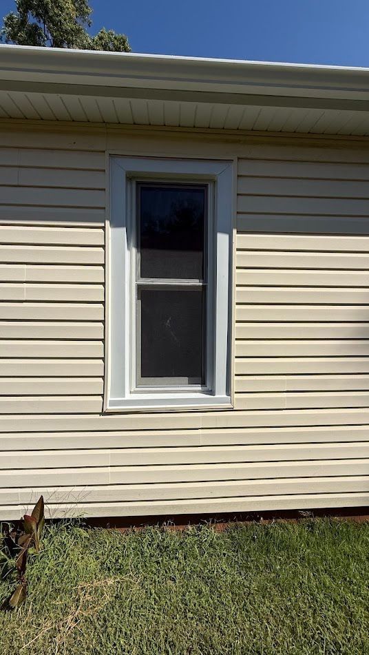 Cream-colored siding with a white-framed window; a sunny day with green grass below.