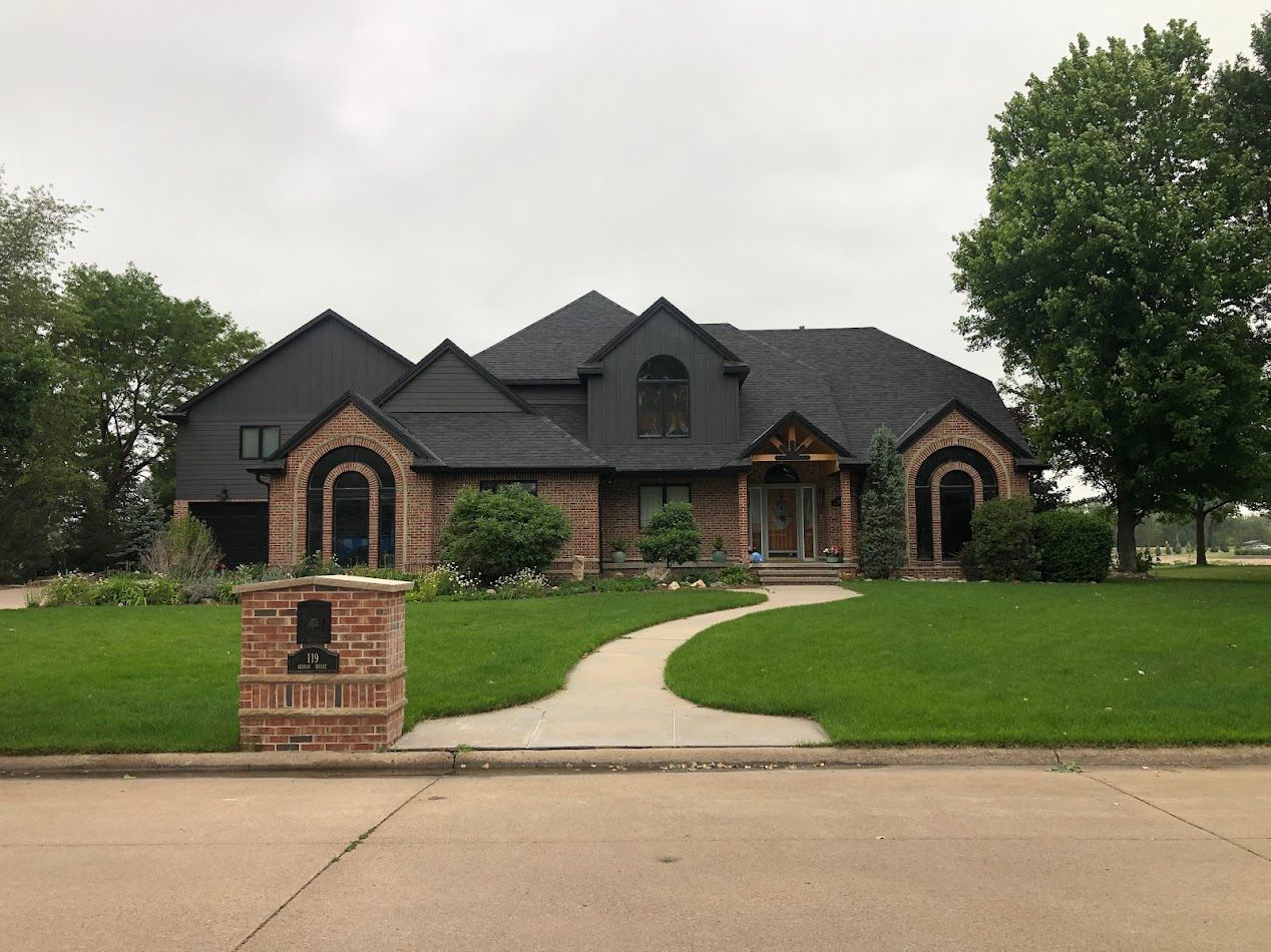Brick and dark-roofed house with arched windows and walkway through green lawn on an overcast day.