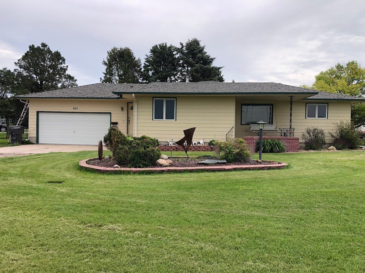 Yellow house with a lawn and small garden bed. Garage and windows. Overcast sky.