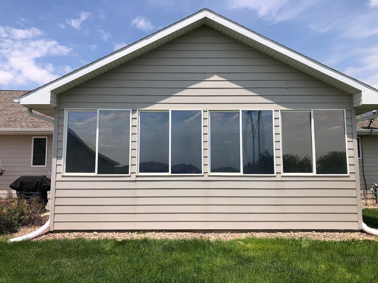 Back of a light gray house with large reflective windows, set on green grass.