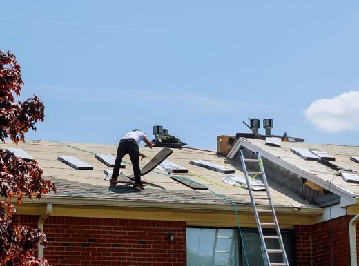 A man is working on the roof of a brick house.