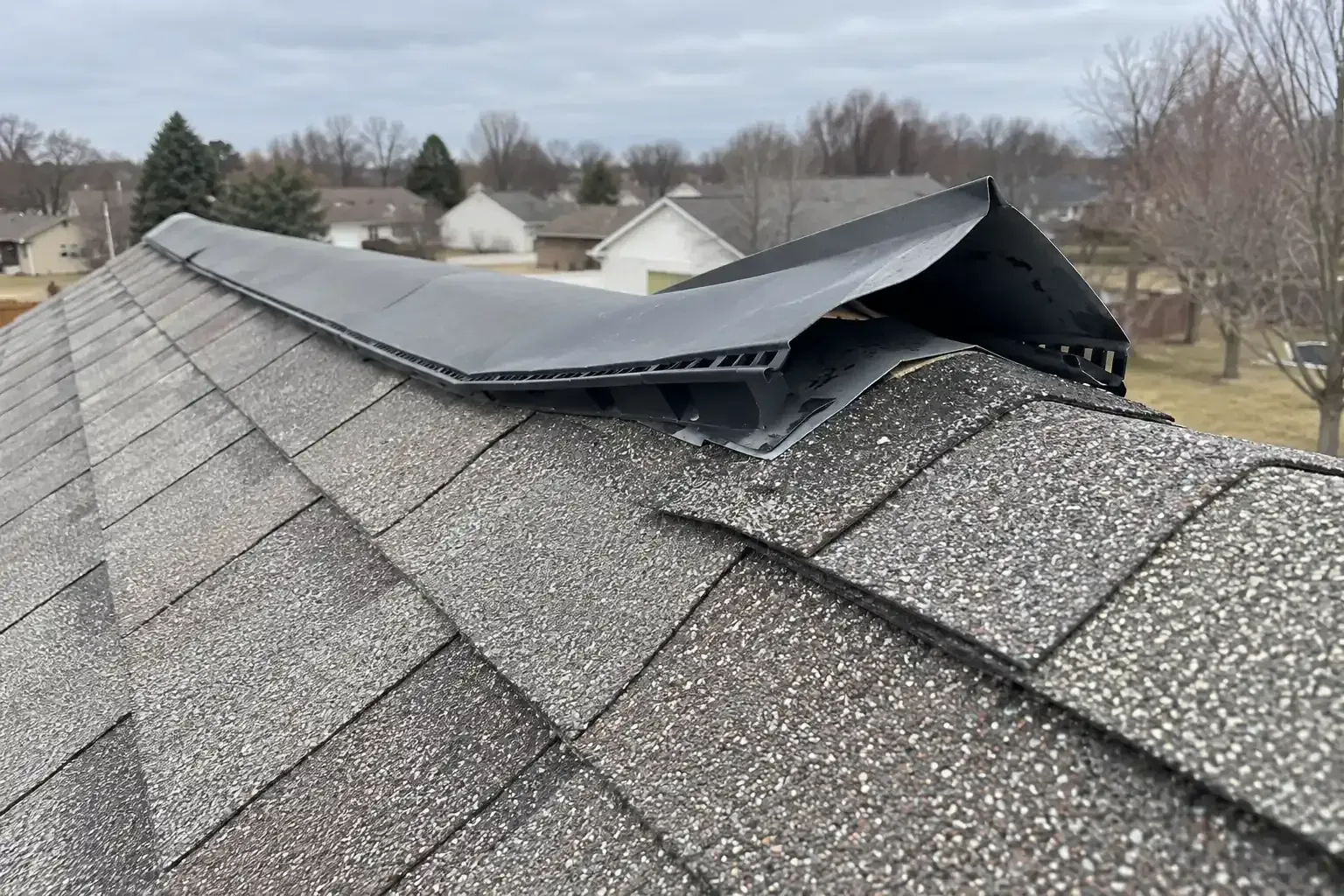 Metal flashing pried up by wind at the edge of a ridge vent
