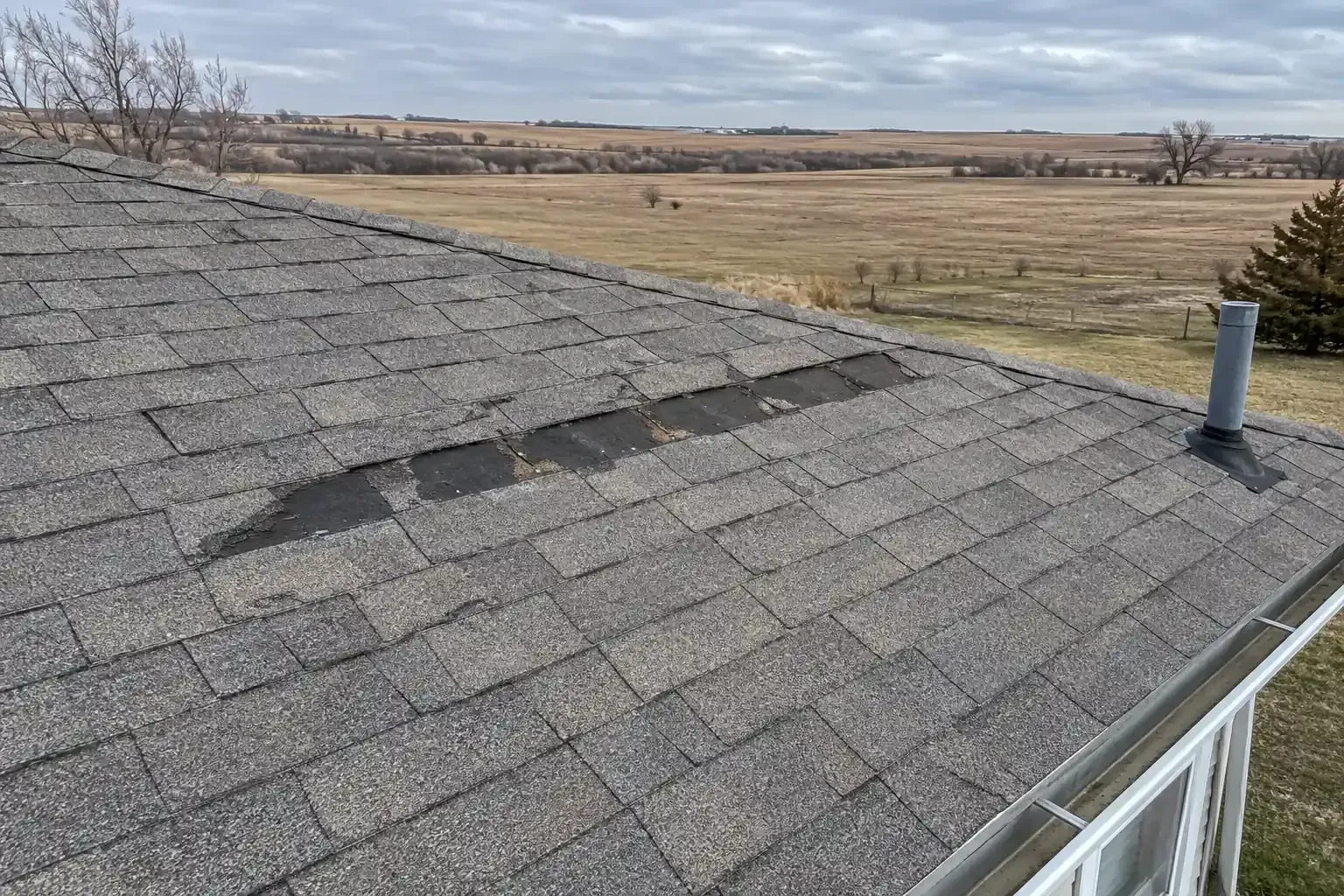 Missing shingle tabs in a row along a windswept asphalt roof