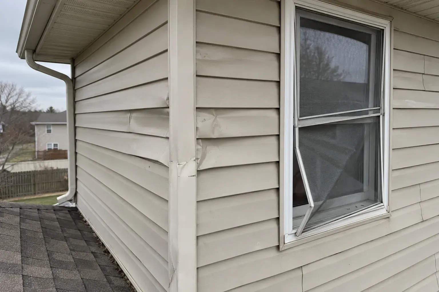 Hail-dented siding and a torn screen on the storm side of a house