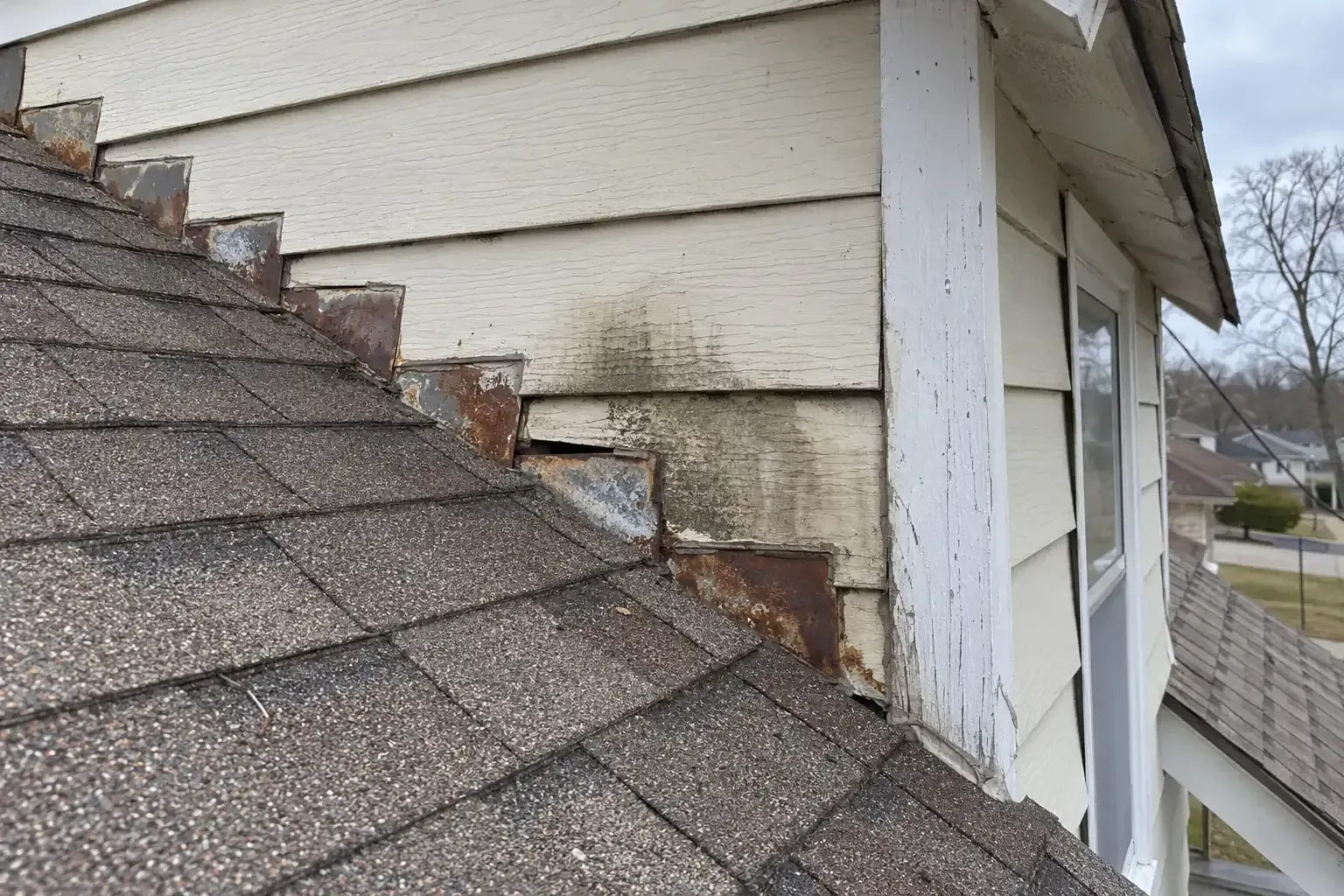 Worn step flashing and water staining where a dormer wall meets the roof