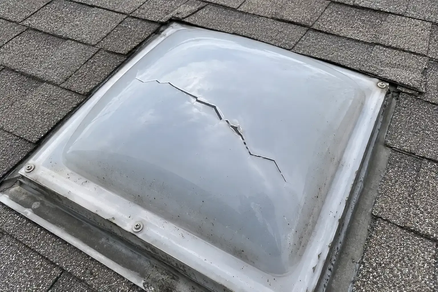 Cracked plastic skylight dome on a shingle roof after a hailstorm