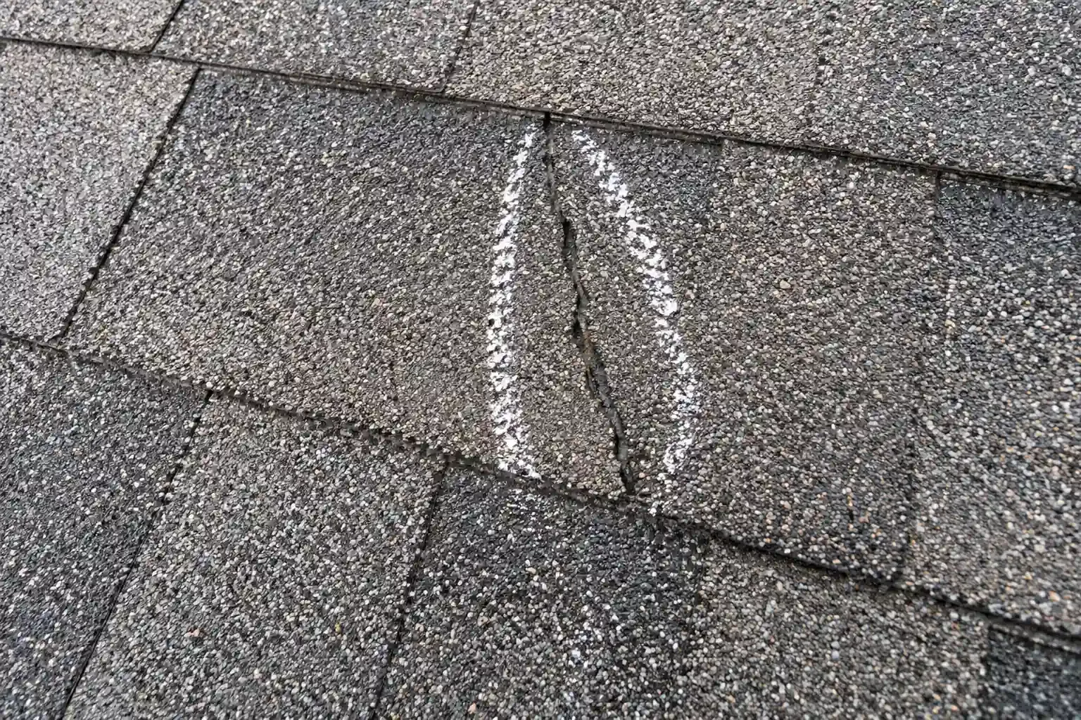 Asphalt shingle split by hail, with the crack marked in chalk