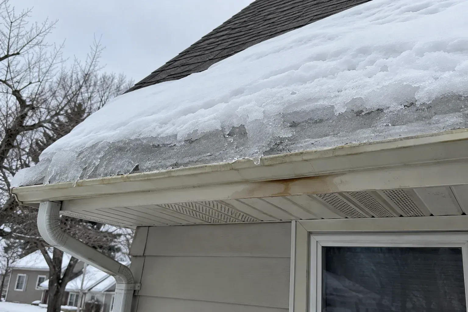 Thick ridge of ice along the eaves of a shingle roof with icicles hanging from the gutter