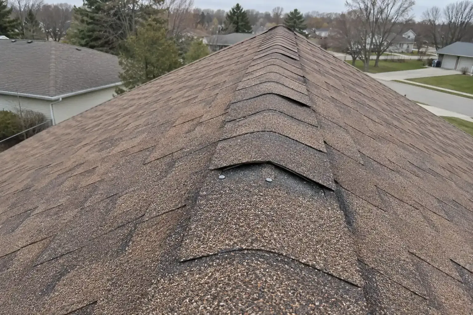Lifted ridge cap shingles along the peak of a roof