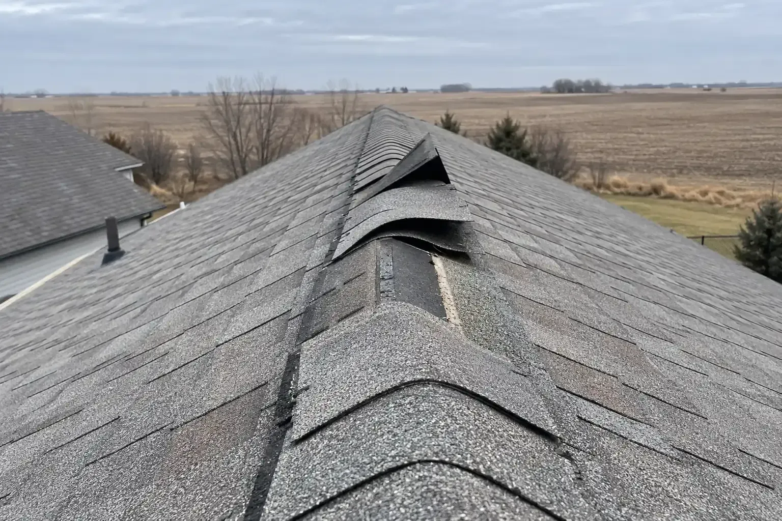 Ridge cap shingles lifted and loosened along the peak of a roof