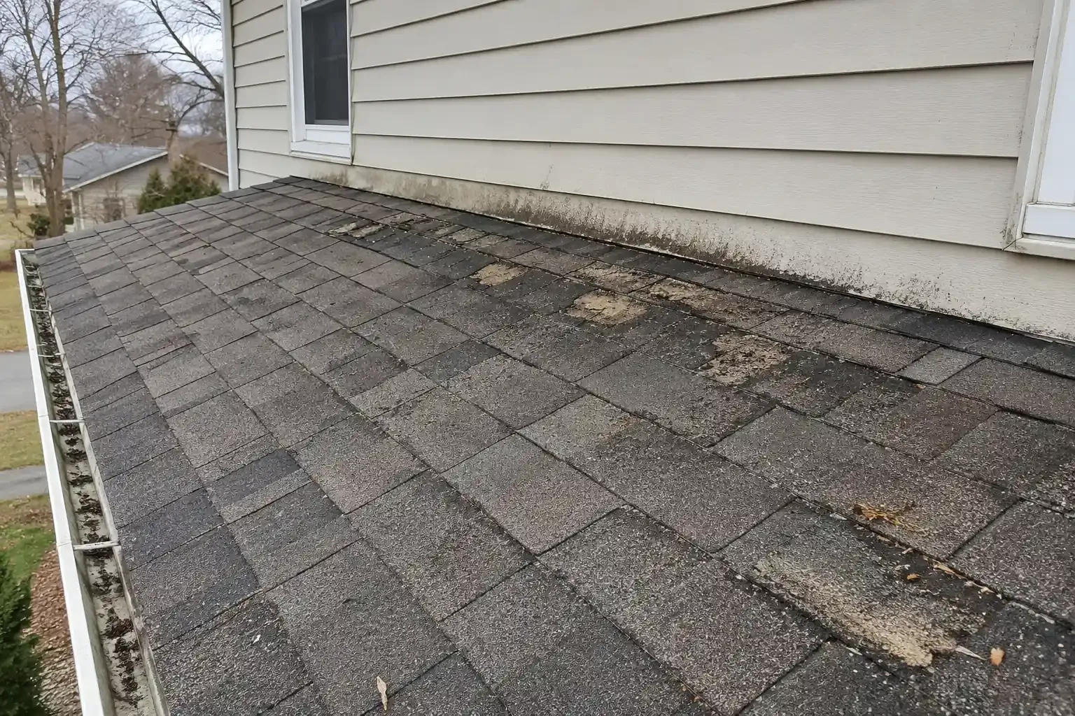 Worn shingles and water stains on a shallow porch roof below a two-story wall