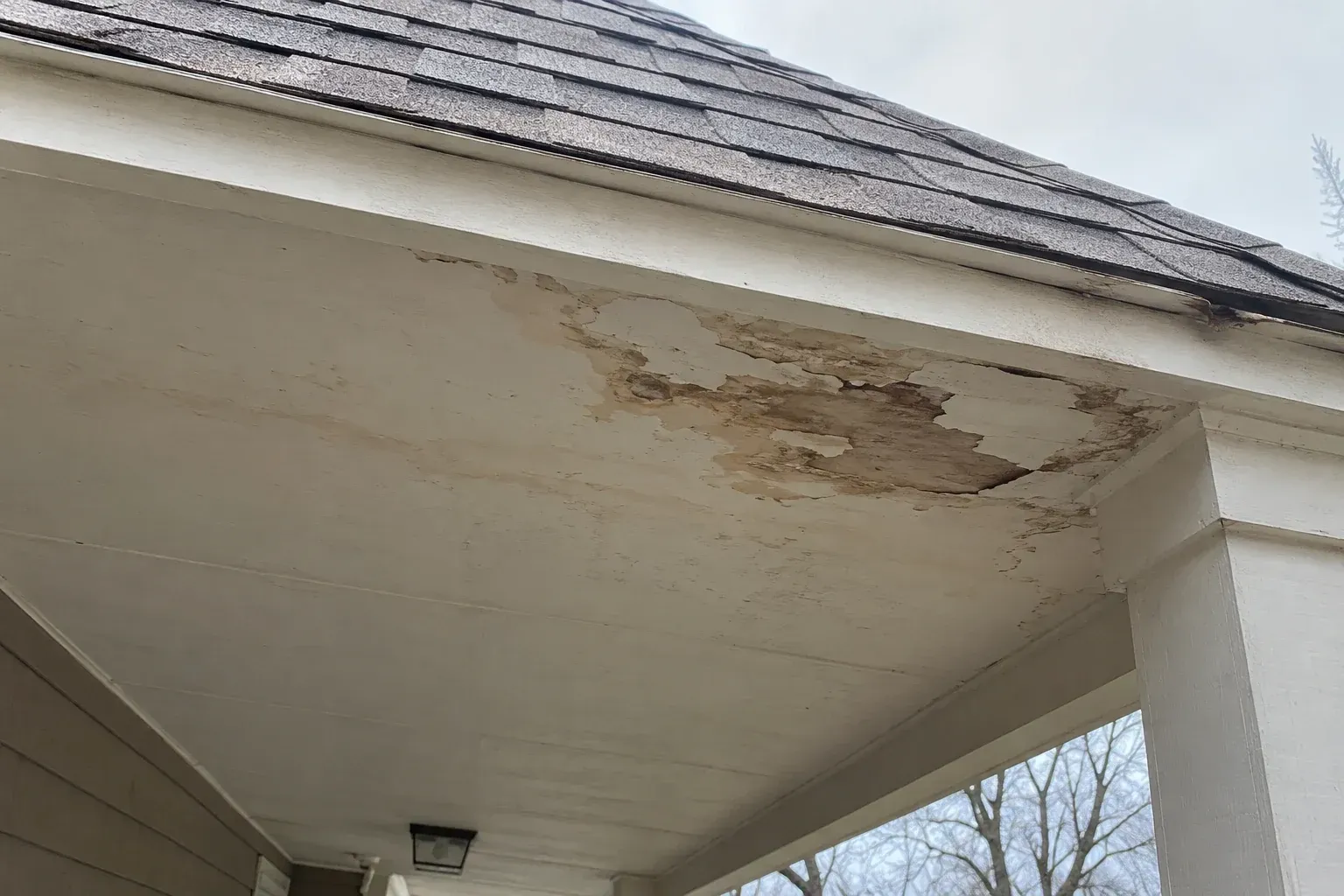 Shallow porch roof with worn shingles above a stained porch ceiling