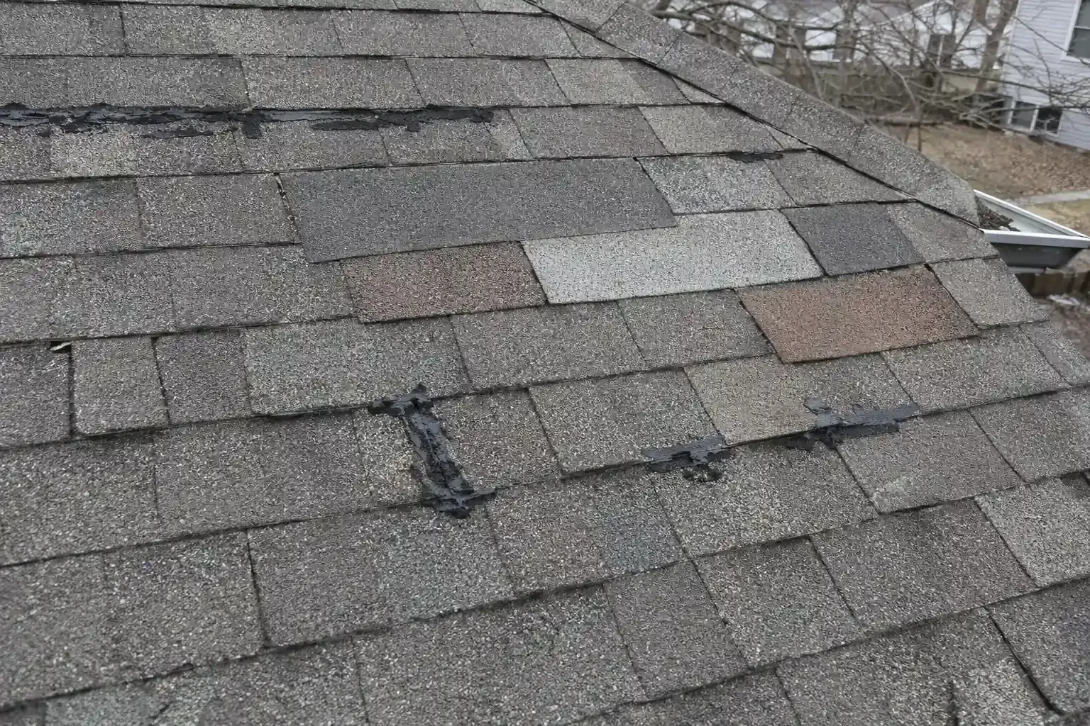 Roof section with mismatched replacement shingles and smears of black roofing tar