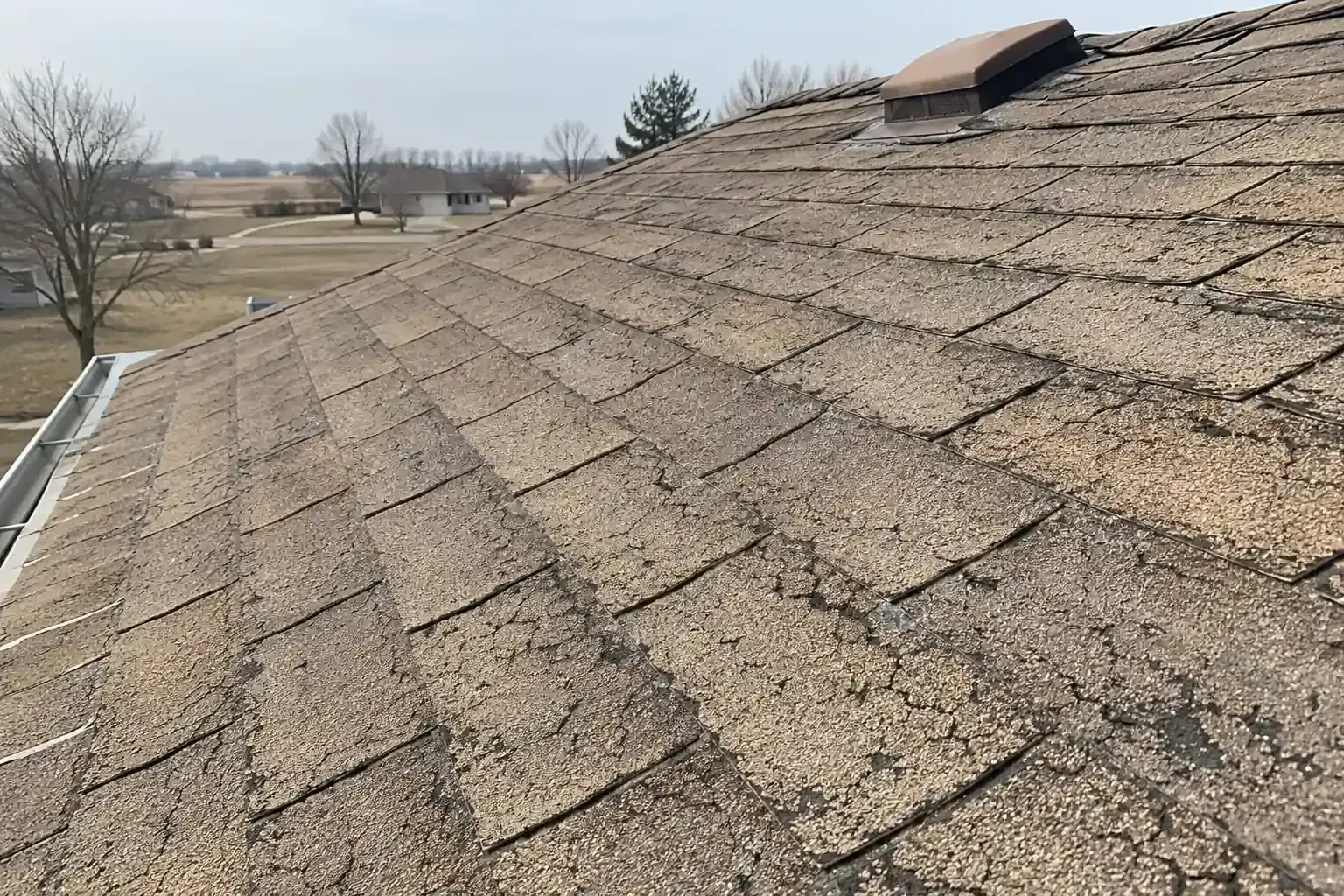 Dry, cracked asphalt shingles with faded color on a sunny roof