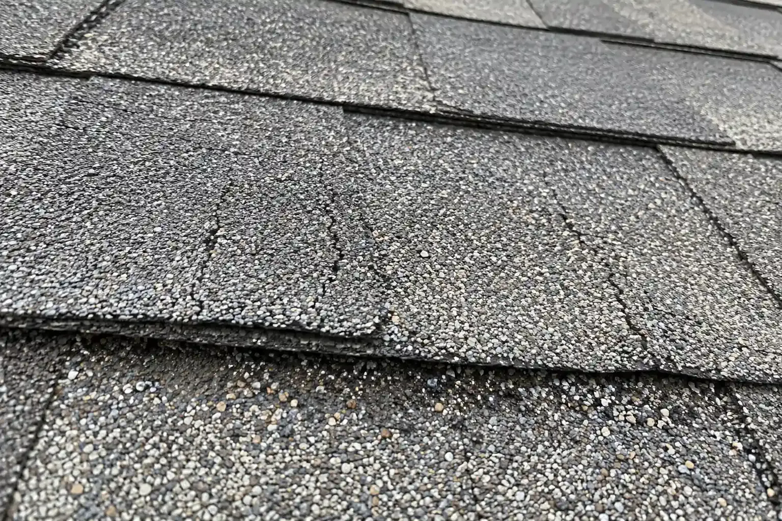 Cracked, sun-faded shingles with granules collecting below them