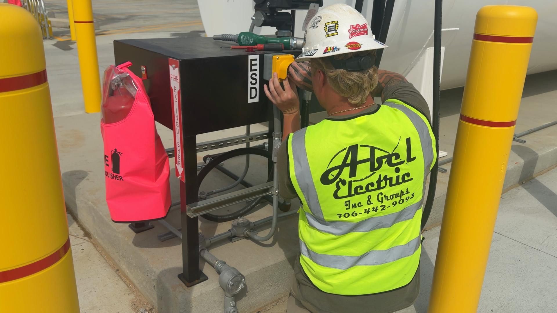 Worker in neon safety vest repairs an electric charging station beside yellow bollards.
