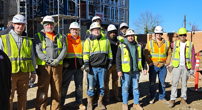Construction crew in hard hats and safety vests posing at a building site under clear blue sky