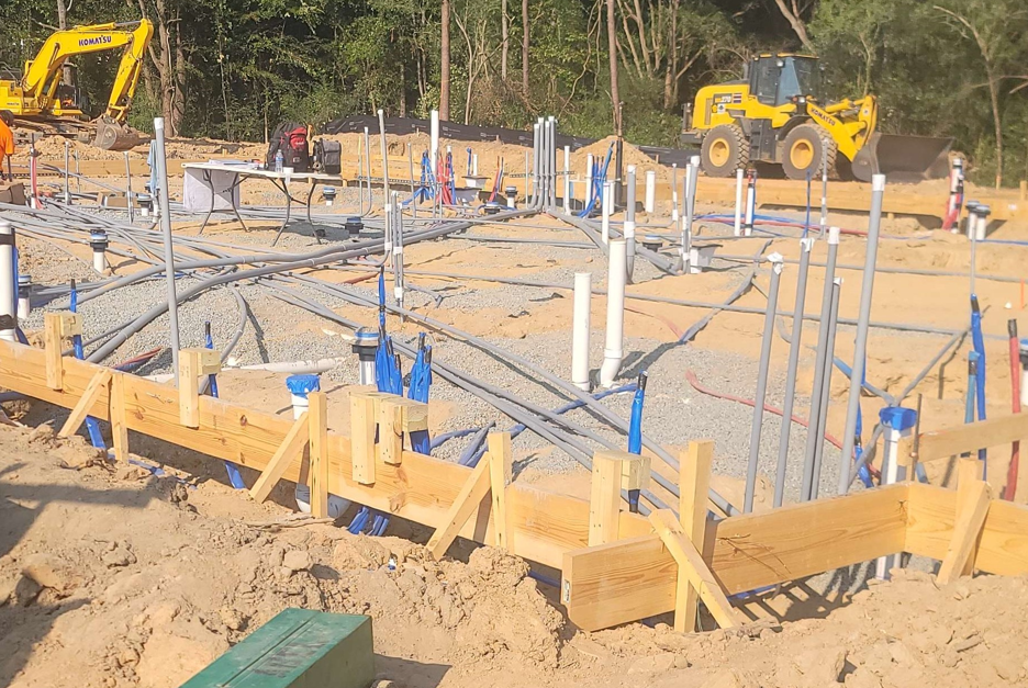 Construction site with excavators, workers, and foundation rebar set in sandy ground