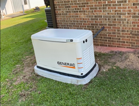 White Generac generator unit beside a brick house on a grassy yard