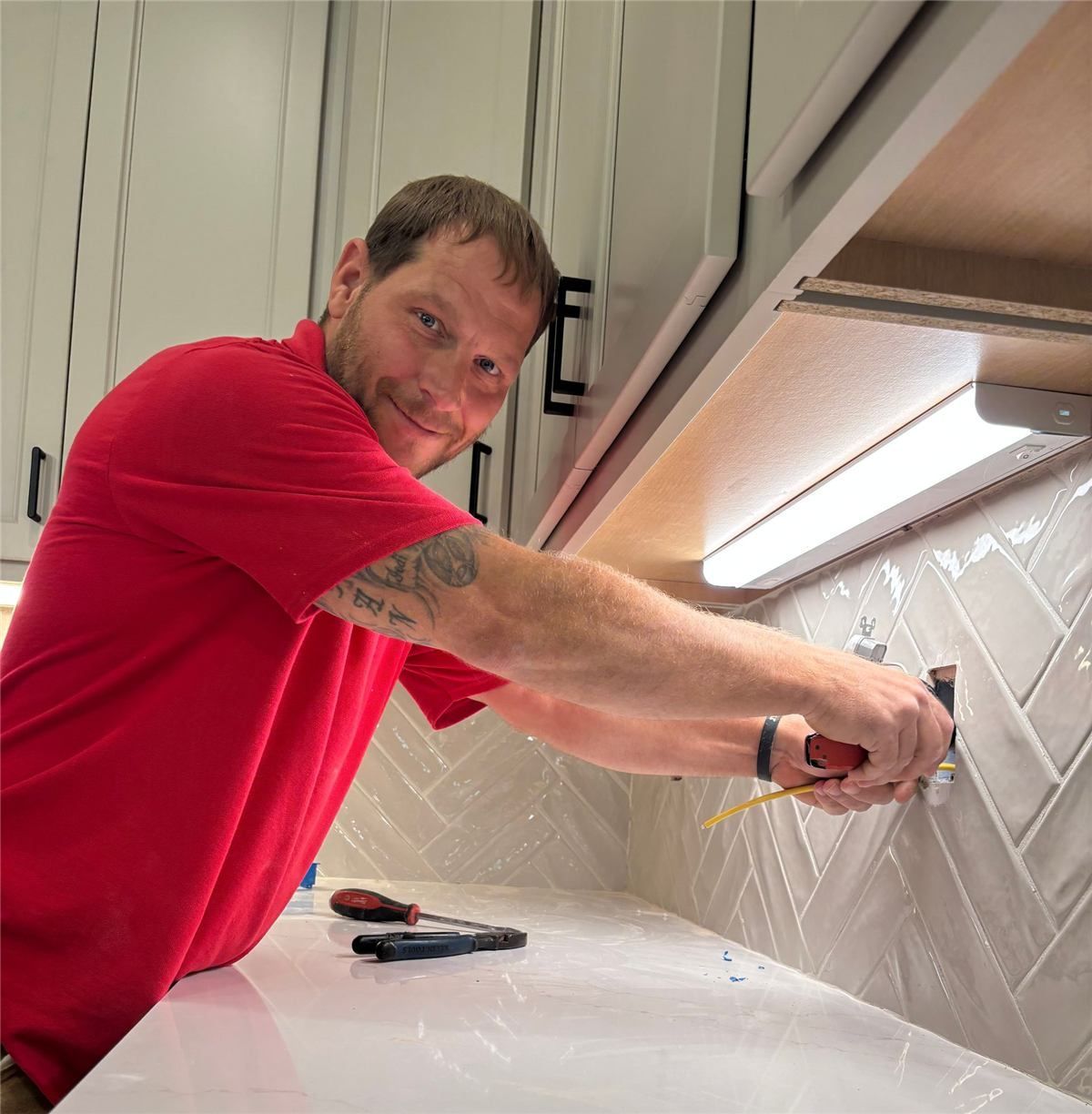 Technician in neon yellow shirt installs hardware inside a cabinet using a drill and screwdriver