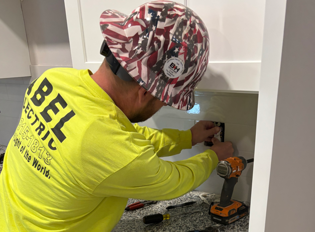 Technician in neon yellow shirt installs hardware inside a cabinet using a drill and screwdriver