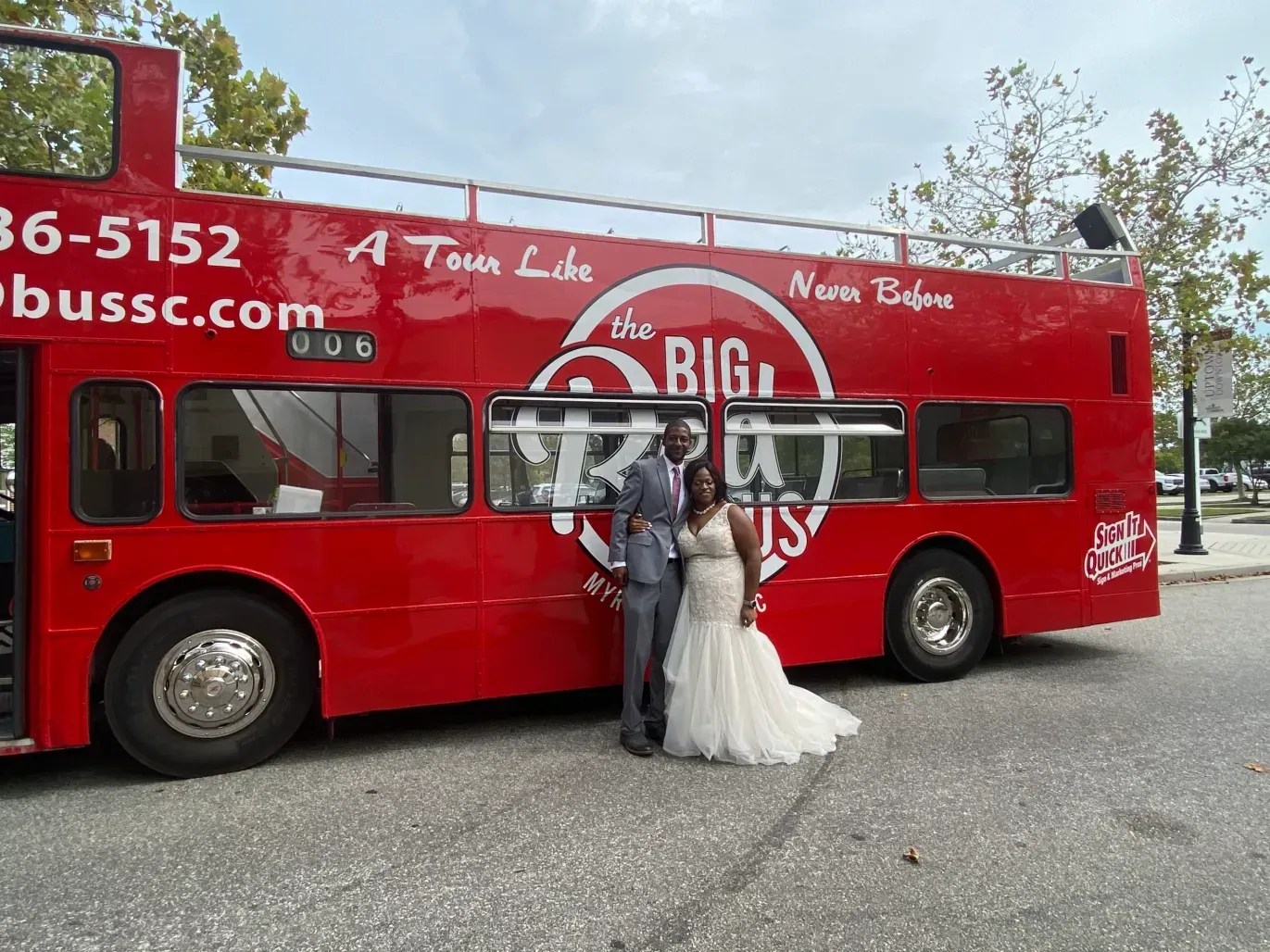 A bride and groom are standing in front of a red double decker bus.
