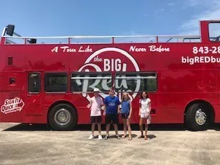 A group of people are standing in front of a red double decker bus.