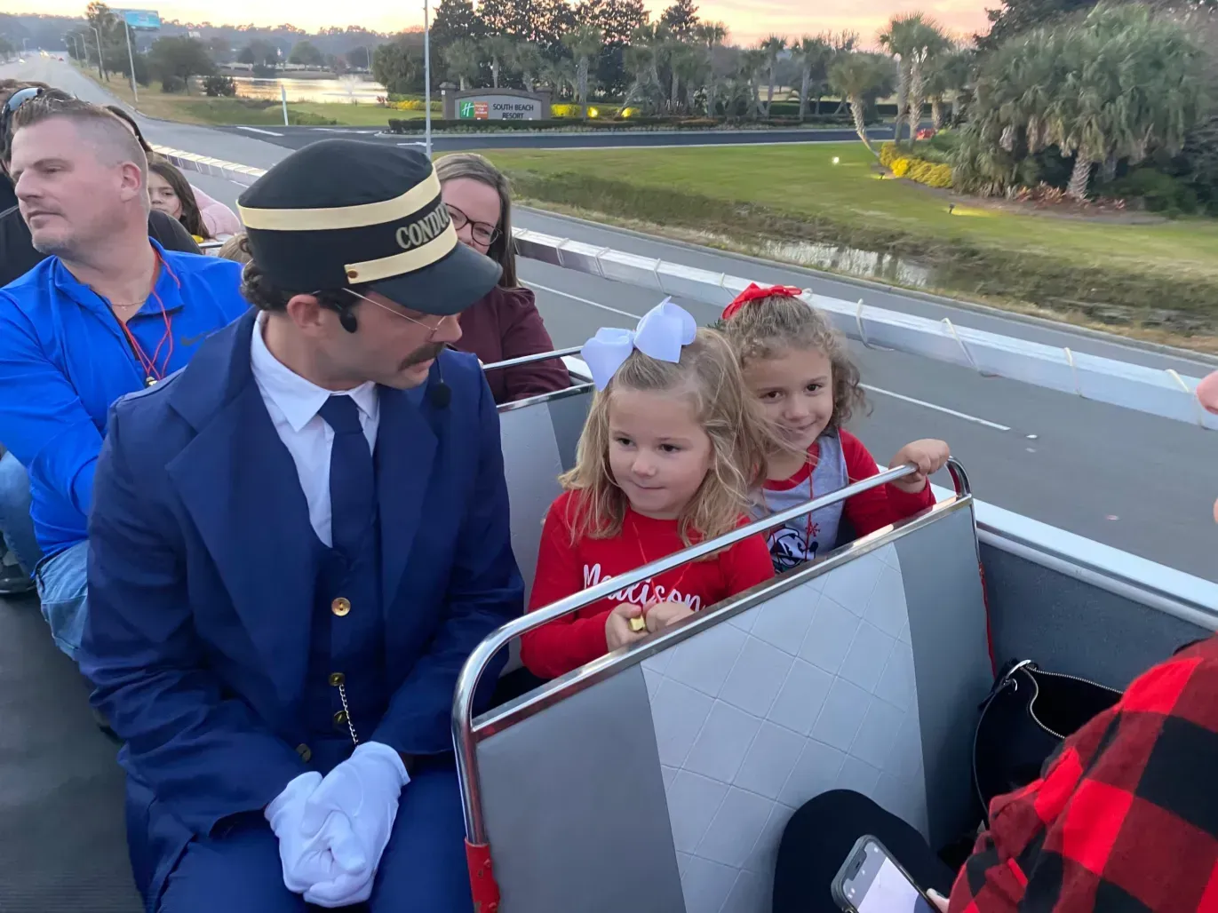 A man in a suit and hat is sitting on a bus with two little girls.