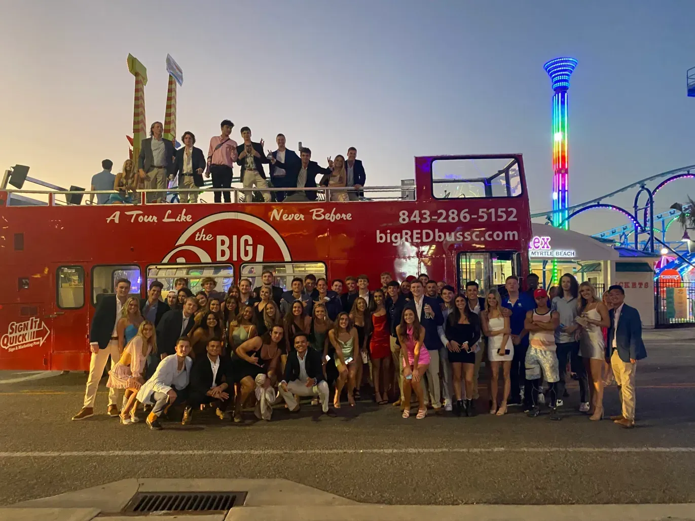 A group of people are posing for a picture in front of a red double decker bus.