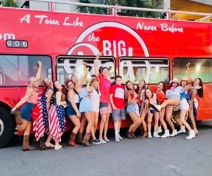 A group of people standing in front of a red bus that says a tour like never before