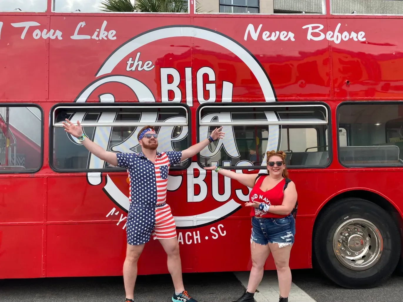 A man and a woman are standing in front of a red double decker bus.