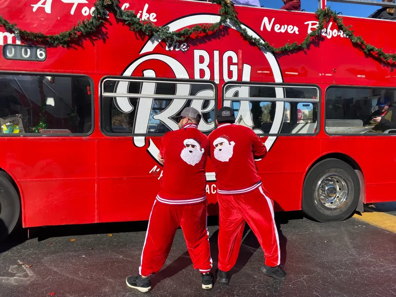 Two men in santa outfits are standing in front of a big red bus