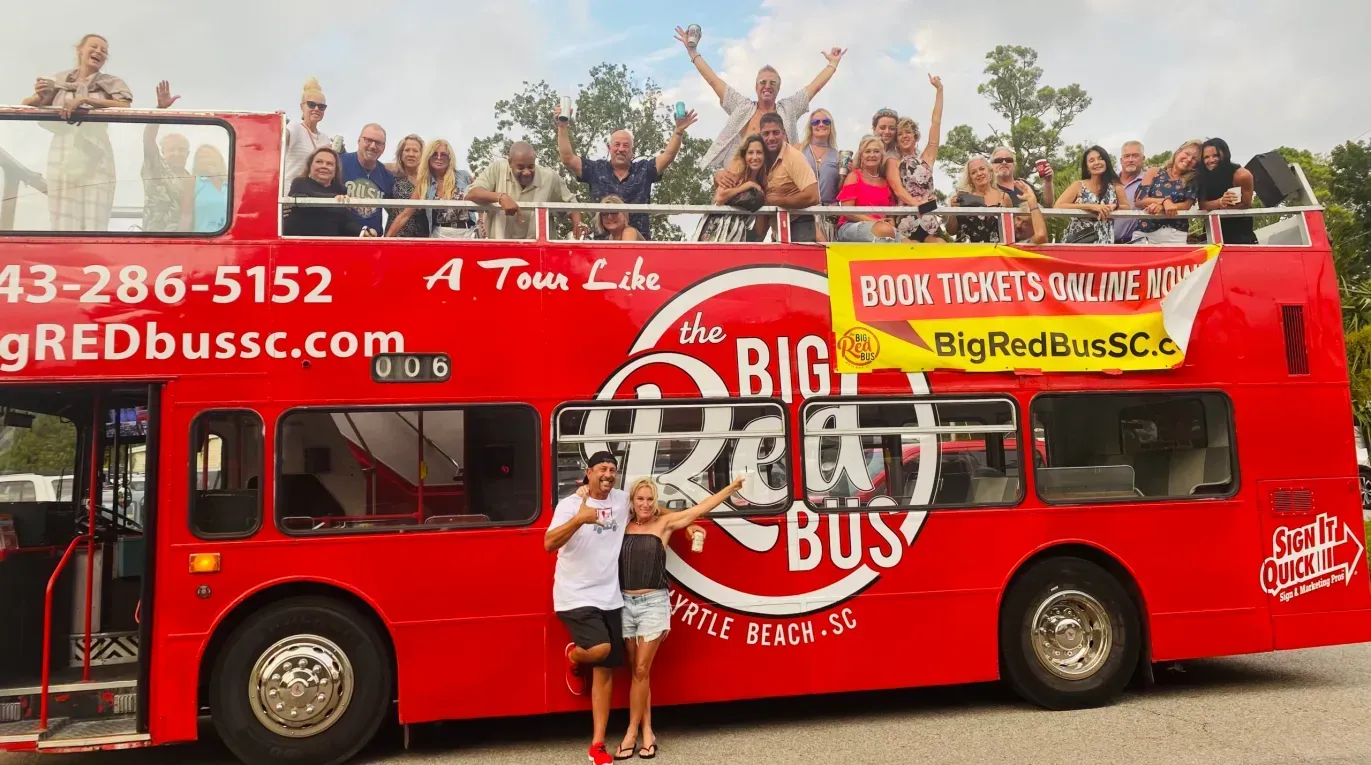 A man is standing in front of a red double decker bus.