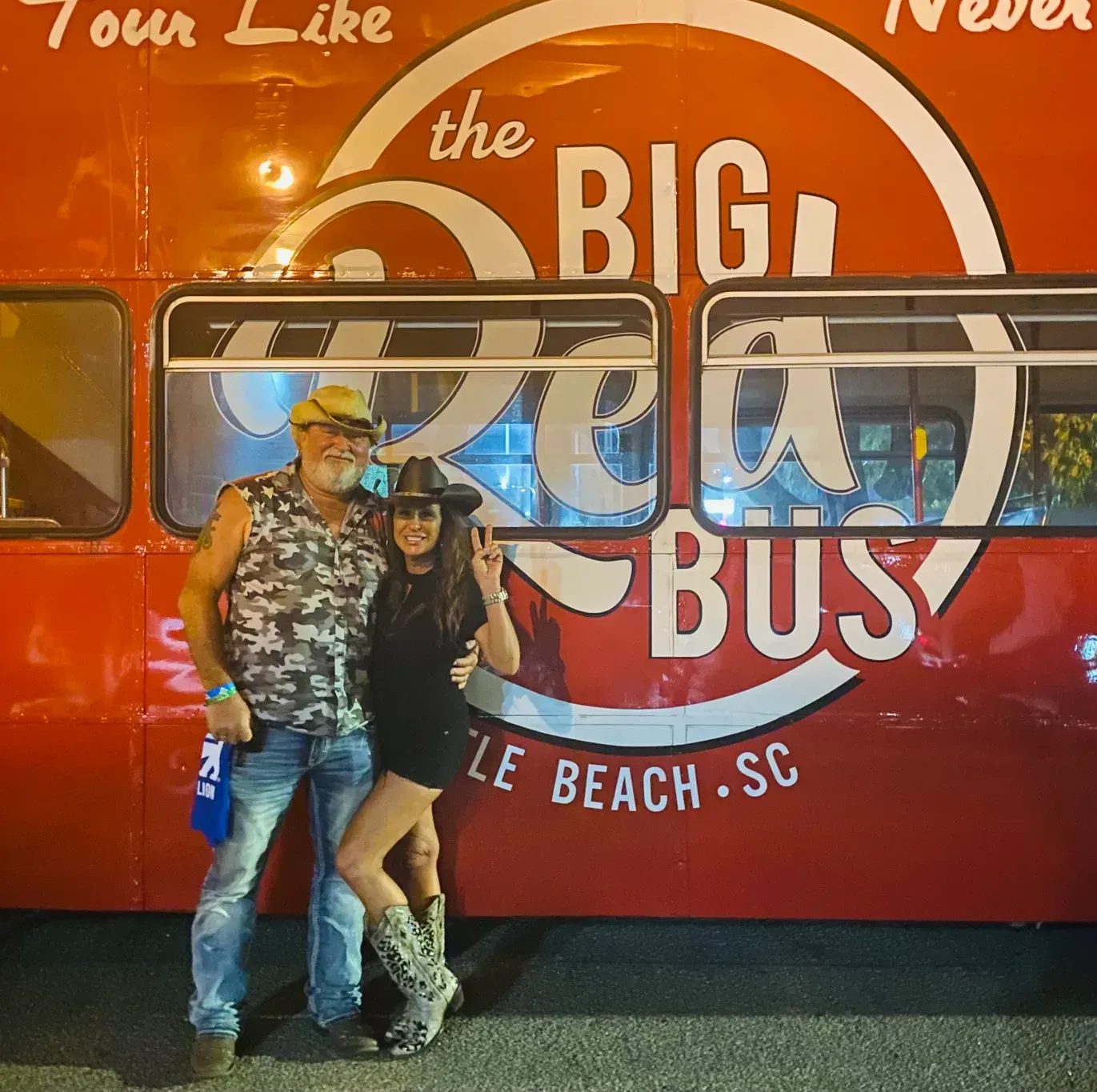 A man and woman pose in front of a big red bus