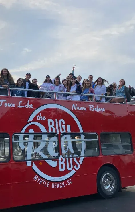 A group of people are standing on top of a red double decker bus.