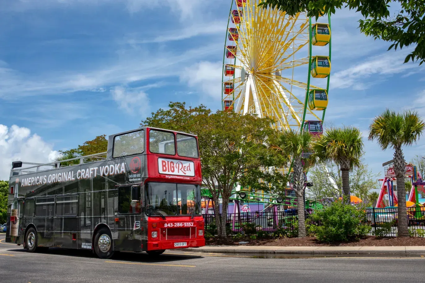 A red double decker bus is parked in front of a ferris wheel.