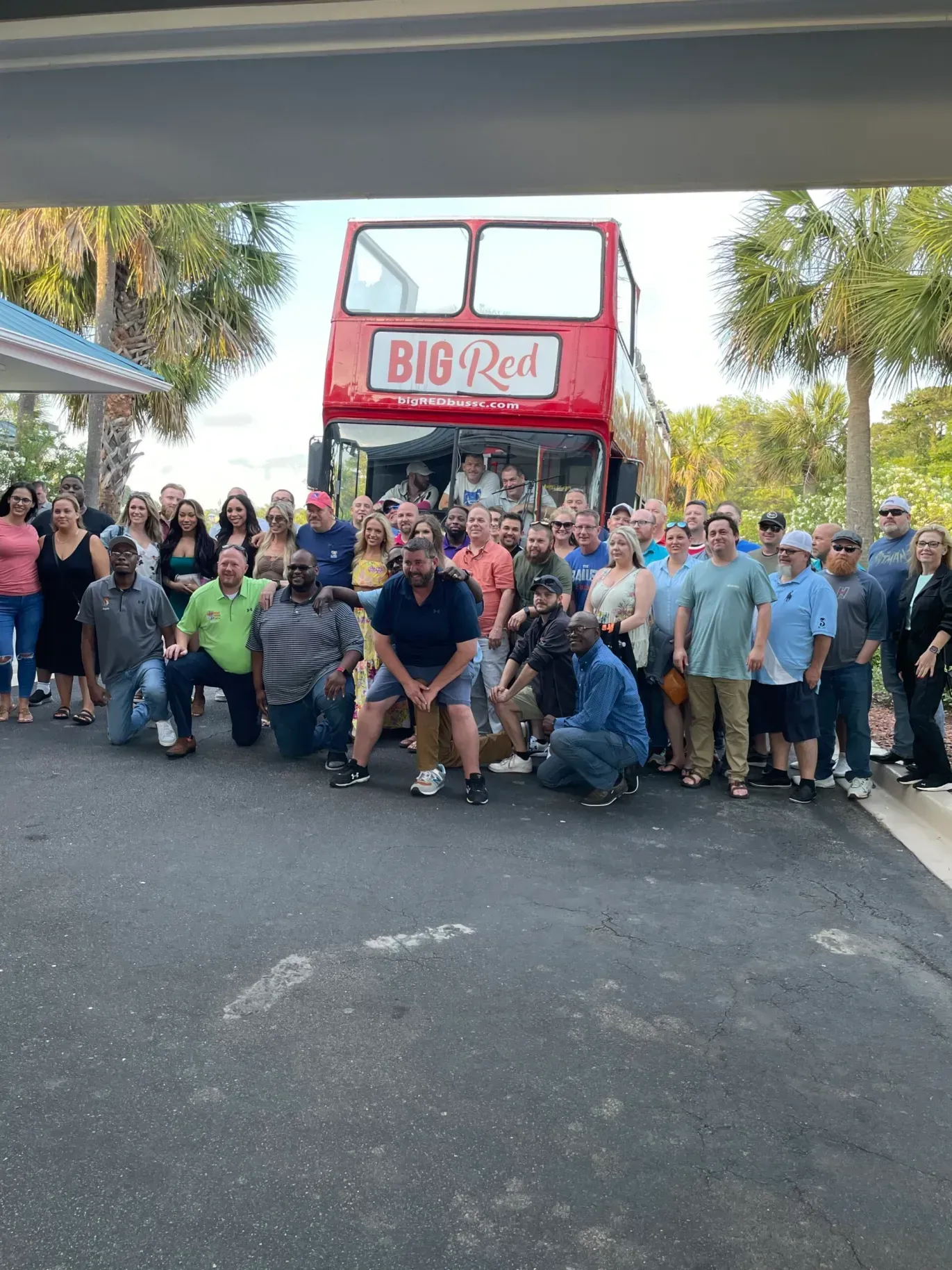 A large group of people are posing for a picture in front of a red double decker bus.