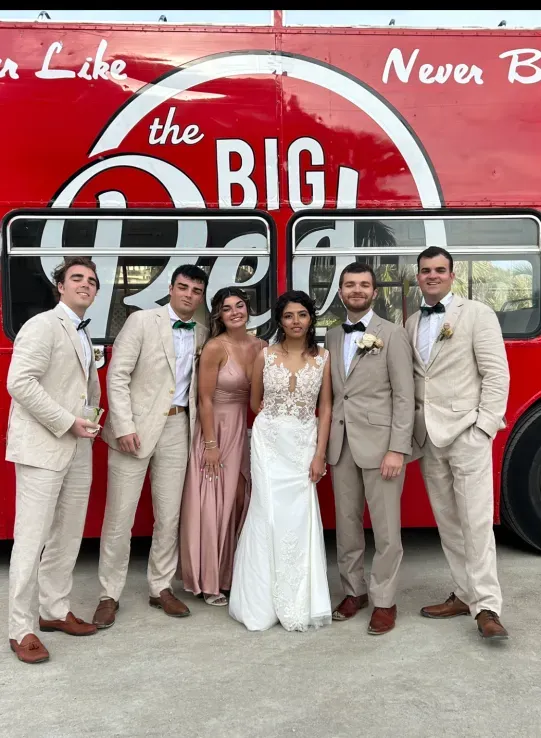 A group of people standing in front of a red bus that says the big people
