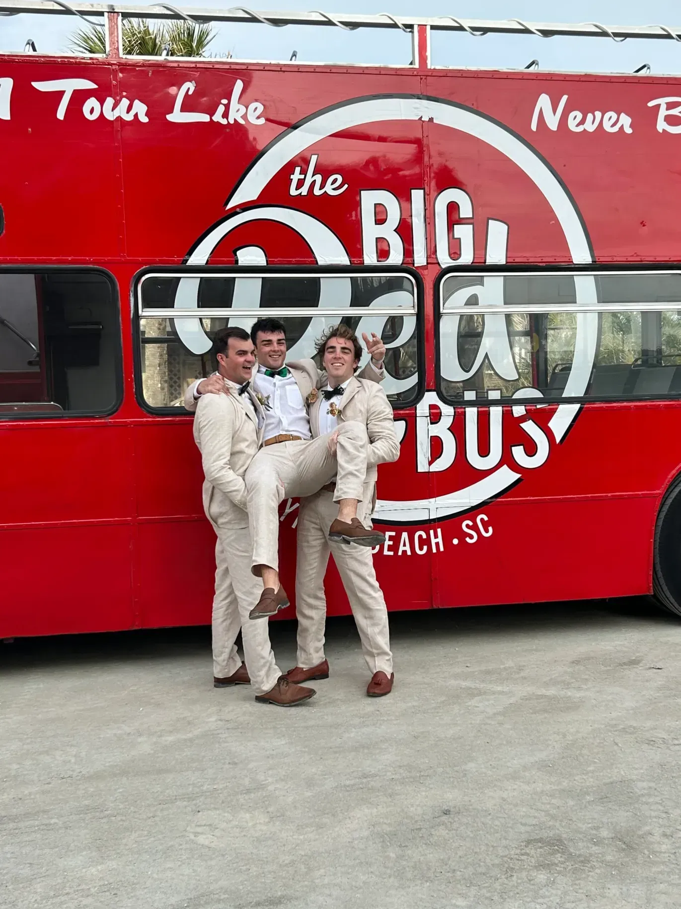 Three men are standing in front of a red bus that says the big bus